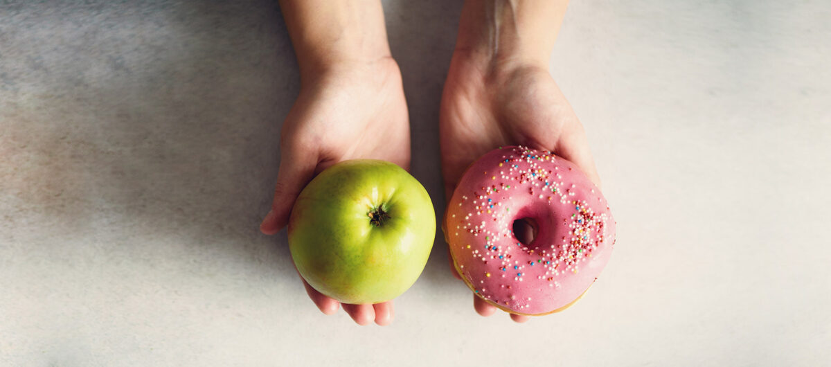 young-woman-in-white-t-shirt-choosing-between-green-apple-and-donut